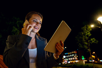 Businesswoman multitasking with phone and tablet during nighttime walk in city
