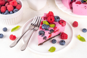 Summer fruit and berry no-baked cheesecake. Creamy whipped cake with chocolate sponge cake, with pink cheese layer, blueberry, raspberry, strawberry, mint leaves, on white table copy space
