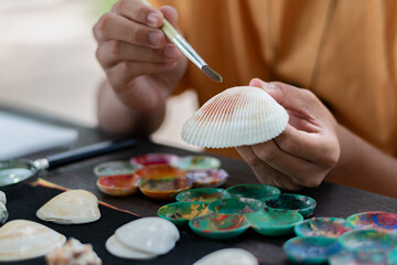 Teenager decorating seashell with paintbrush during art class, creative hobby and craft activity for kids and students.
