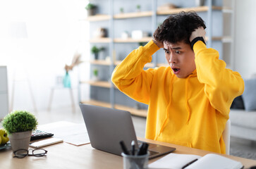 Deadline Concept. Portrait of shocked scared asian guy sitting at desk with laptop, screaming and...