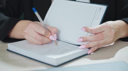 close up of adult woman with polished pink nails writing in diary using ballpoint pen while holding notebook open on desk in bright office environment