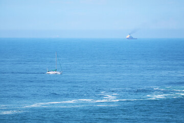 Impressive blue Atlantic ocean with a white yacht and a cargo ship in afar