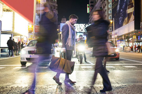 Man holding bag and cell phone crossing a street at night