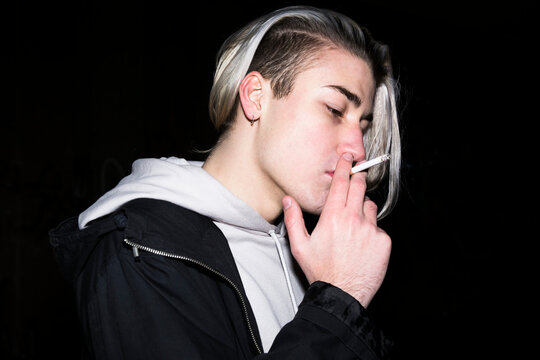 Young man smoking cigarette in front of black background