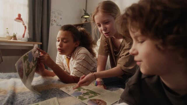 Diverse group of cheerful kids chatting playing game while pointing at leaflet with map in cozy bedroom during summer vacation