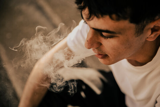 Young man blowing out smoke from marijuana joint