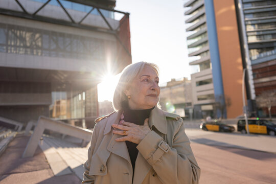 Woman in trench coat taking a selfie during sunset in an urban setting