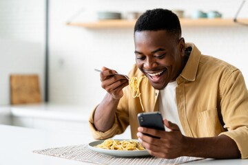 A man enjoys a delicious pasta meal while using a smartphone in a cozy kitchen setting