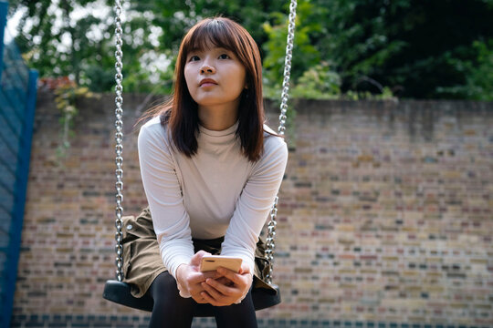 Young woman sitting with smart phone on swing at playground