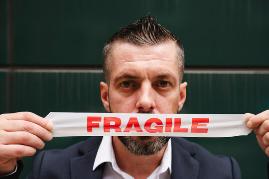 Businessman covering mouth with fragile tag in front of wall