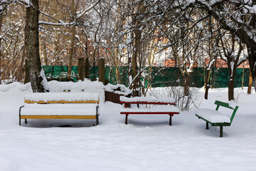 Three colorful benches covered with snow in empty winter park.