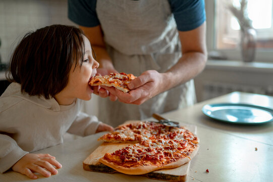 Man feeding pizza to son in kitchen at home