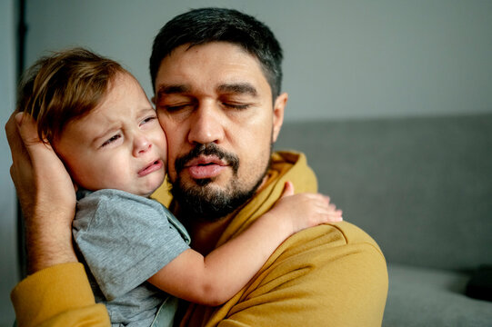 Father embracing crying son in living room at home