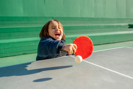 Cheerful boy playing table tennis on sunny day