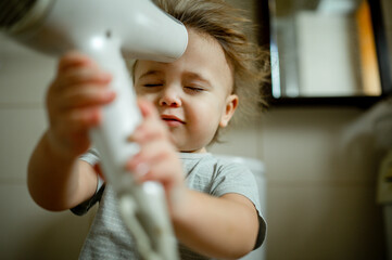 Boy with eyes closed blowing hair with dryer at home