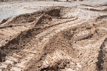 a rugged landscape of freshly disturbed soil, marked by tire tracks and earthy textures, suggesting recent construction or excavation activity under a bright, natural light, disrupted, surface
