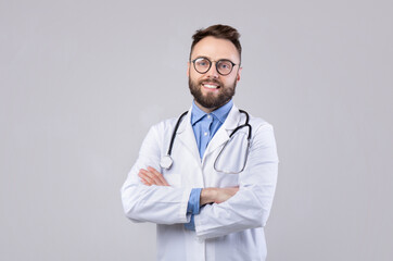 Portrait of happy young doctor in lab coat standing with crossed arms and looking at camera over...