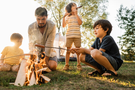 Father and children roasting sausages in bonfire at picnic