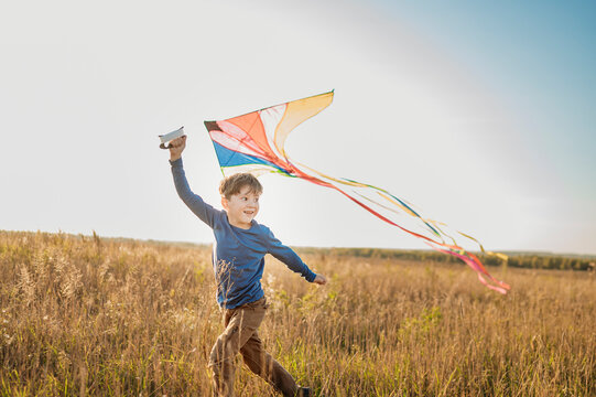 Smiling boy flying kite and running in field under sky