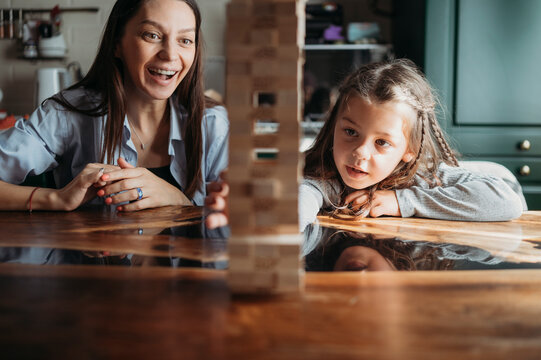 Smiling mother watching daughter playing block removal game at table
