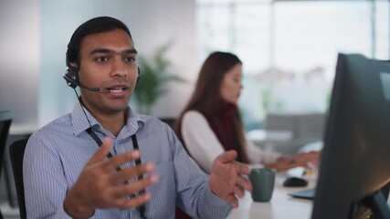 Focused indian man at busy tech customer support call center, confidently offering expert solutions and dedicated assistance for customer using headset and computer