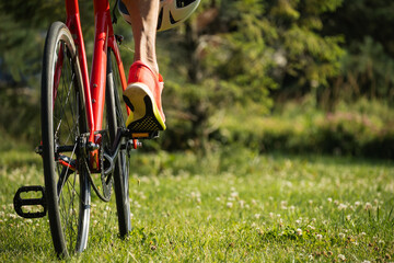 Close up of leg stand on red bike pedal on green grass. Foot on pedal of bicycle. Bike sport Side back. Summer season. Cycling outdoors