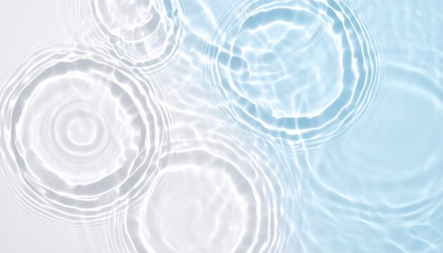 Ripples and concentric circles form on a clear water surface as droplets gently fall, creating soothing patterns and reflections in pale blue hues.