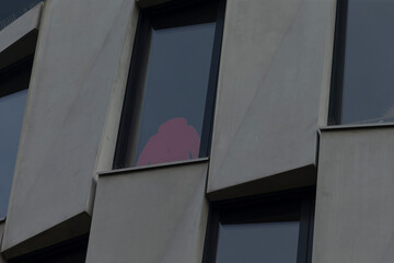 A person stands and looks out from a window of a tall building, observing the surroundings from...
