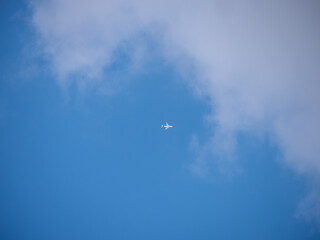 Airplane flying high in a blue sky with scattered clouds, captured from the ground with minimal composition and soft daylight.