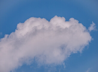 White fluffy clouds in a blue sky on a sunny day, captured from below with soft natural light.
