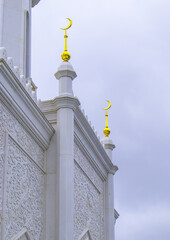 The walls of the mosque with golden crescents and carved white marble walls against the backdrop of a cloudy dawn sky