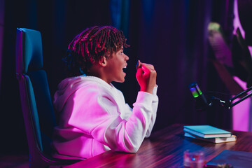 Young gamer and online blogger streaming live with vibrant neon lighting and high-tech setup...