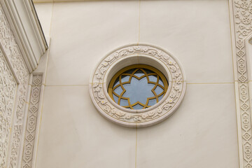 A round window with floral ornamentation and a carved frame on the white marble wall of the mosque