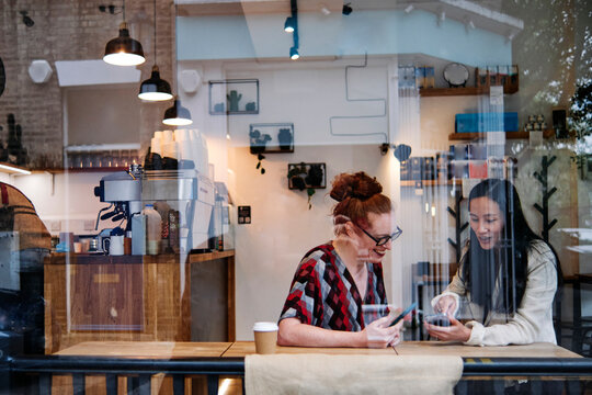 Woman showing mobile phone to female friend in cafe