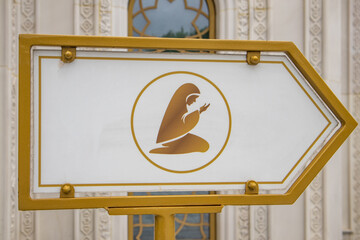 A sign indicating the place of prayer and depicting a Muslim woman, against the backdrop of a mosque wall