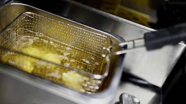 Top view of commercial fryer, metal basket with food frying in hot oil, bubbling intensely.