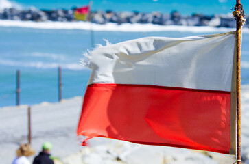 A vibrant red and white flag is flying proudly on a tall pole on a beach