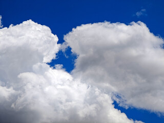 Bright white clouds drift across a clear blue sky on a sunny day in early afternoon hours
