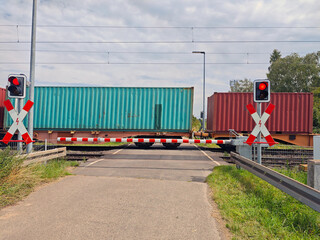 Train crossing gates blocking road with freight containers passing during daylight hours