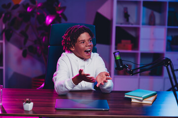 Teen blogger recording podcast at home desk with microphone and colorful neon lights enhancing the...