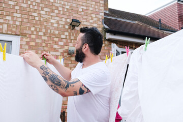 Tattooed man drying sheet on clothesline at back yard