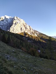 A stunning alpine scene showcasing a sunlit mountain partially dusted with snow, rising above a...