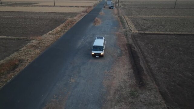 Aerial view of a lone van parked on a gravel patch alongside a long road near Shinakafuchigawa Bridge amidst fields, Fujiokaminami, Shizuoka, Japan.