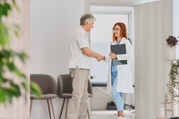 A medical professional warmly welcomes an elderly man in a clinic, promoting trust. Representation...