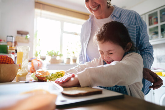 Happy mother and daughter preparing sandwich at home