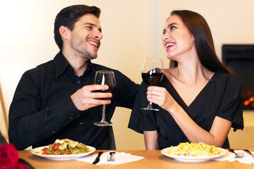 Romantic Moments. Happy loving man and woman sitting at table in cafe or at home, drinking red wine, holding glasses, having dinner celebrating St Valentine's Day or anniversary, talking and laughing