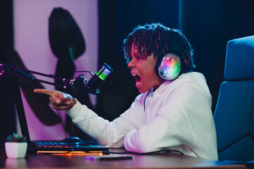 Excited young gamer wearing headphones streaming online in a vibrant home studio setup with neon...