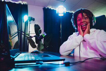 Young male gamer and vlogger using a professional setup with neon lights, expressing excitement...