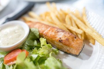 Salmon fillet steak served together with vegetable, french Fries and dipping sauce on white dish