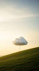 A fluffy white cloud floating over a green grass hill being held by a red string or piece of yarn, surreal scene